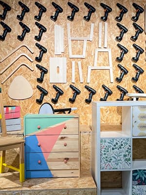 Eine Kommode aus Holz, die angemalt wurde und ein weißes Regal stehen vor einer Holzwand an der dekorativ Akkuschrauber aufgehängt sind.