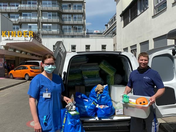 Eine Krankenschwester und ein IKEA MItarbeiter stehen vor einem Lieferwagen mit Spenden für das Kinderspital