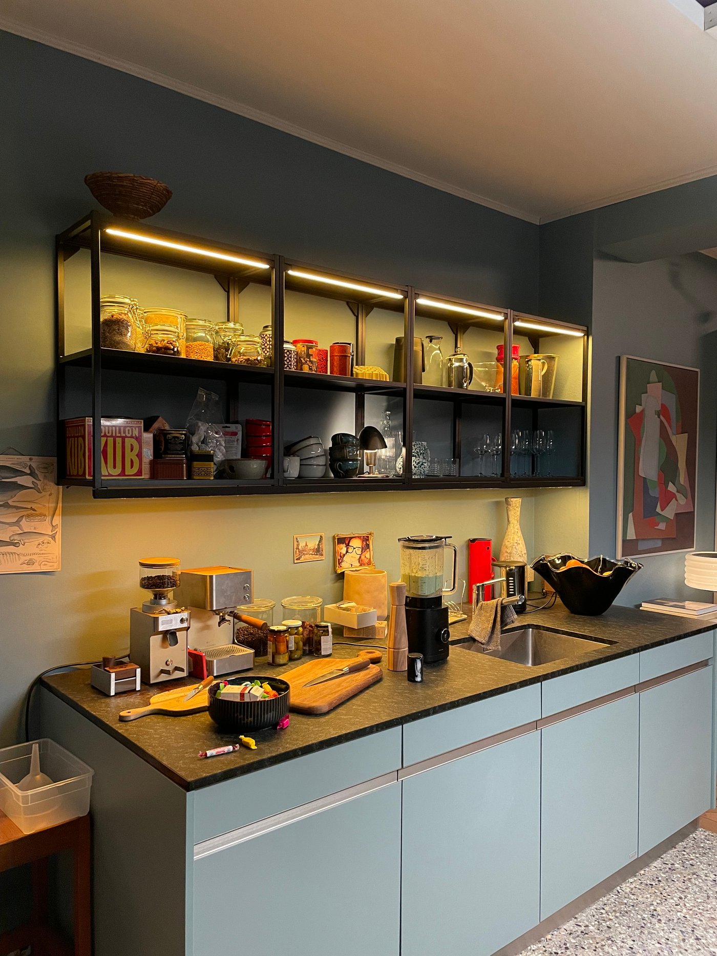 Eine Küchenzeile mit verschiedenen Küchenutensilien auf der Arbeitsläche und offenen Küchenregalen an der Wand.