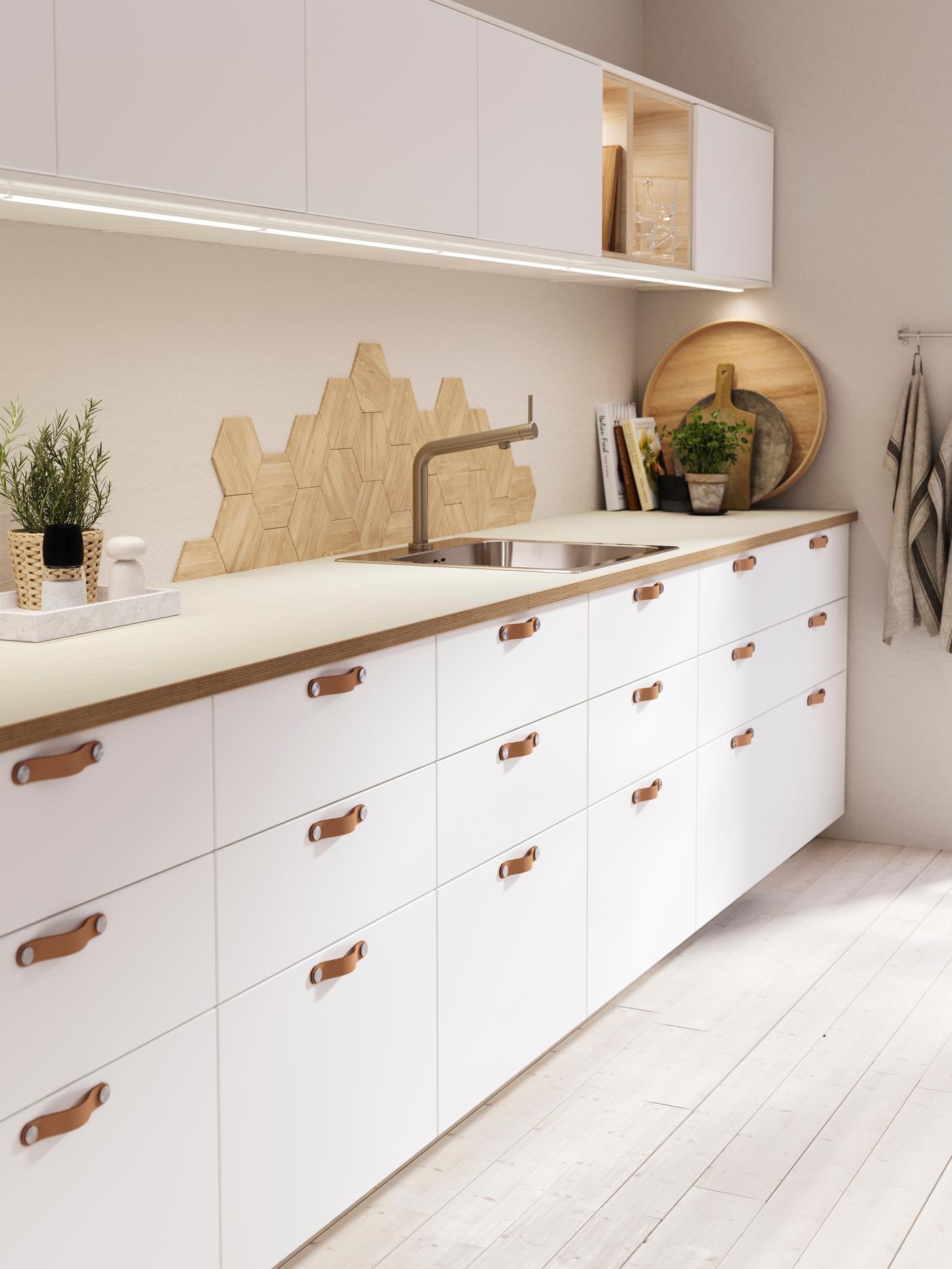 Eine Küchenzeilenlösung mit weißen Fronten und einer weißen Arbeitsplatte, Darauf eine Deckopflanze.