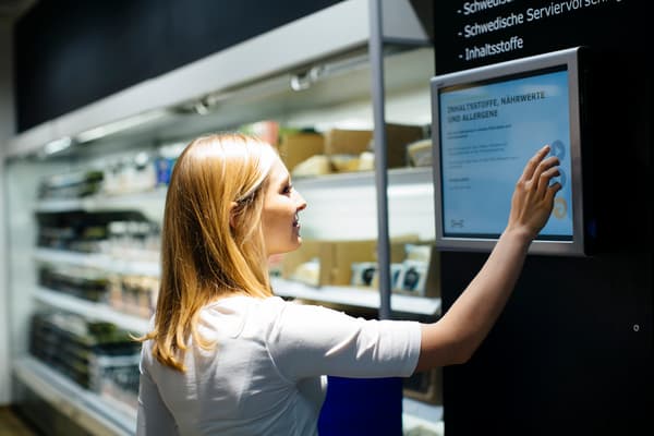 Eine Kundin schaut auf einem digitalen Display die Inhaltsstoffe, Nährwerte und Allergene nach.