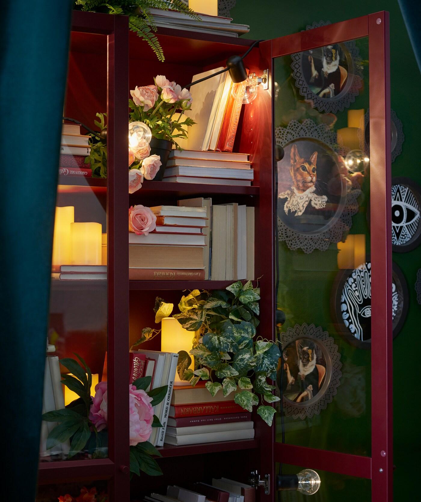 Eine Lichterkette wie IKEA SVARTRÅ LED-Lichterkette in einem Regal, wie hier BILLY Bücherregal mit Glastüren in Dunkelrot, sorgt des Nachts für eine geheimnisvolle Stimmung.