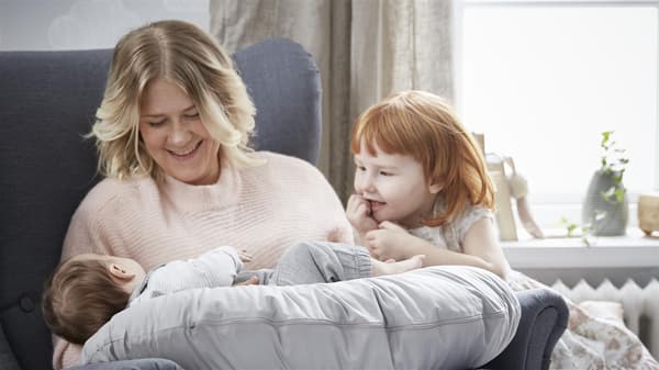 eine Mutter und ihre Töchter in einem Hocker, das Baby liegt auf der Schoß der Mutter in einem Baby Kissen