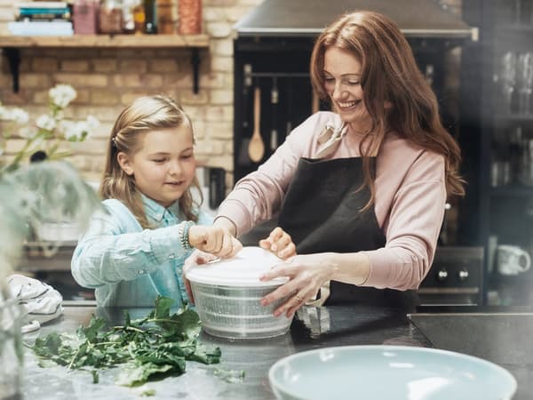 Eine Mutter zeigt ihrem Kind wie es die UPPFYLLD Salatschleuder bedient.