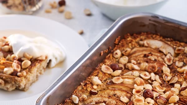 Eine Ofenform mit HJÄLTEROLL Körnermischung steht neben einem weissen Teller mit etwas Porridge und einem Klecks Joghurt darauf.