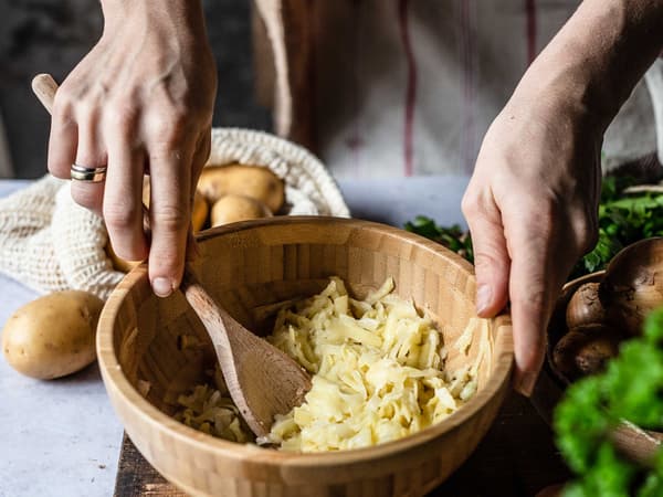 Eine Person bereitet den Teig für Kartoffel-Zwiebel-Rösti zu.