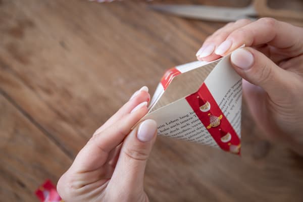 Eine Person faltet aus einem Stück Papier eine Geschenktasche ein Dreiecksform.