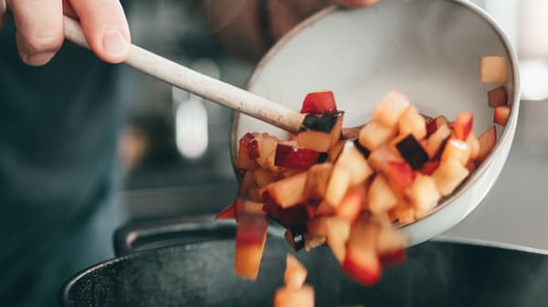 Eine Person gibt Gemüse in einen Topf, um die Soße für PLANTBULLAR Albóndigas vorzubereiten.