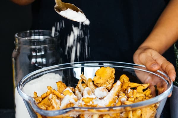 Eine Person gibt Mehl in eine Schüssel mit Pfifferlingen.