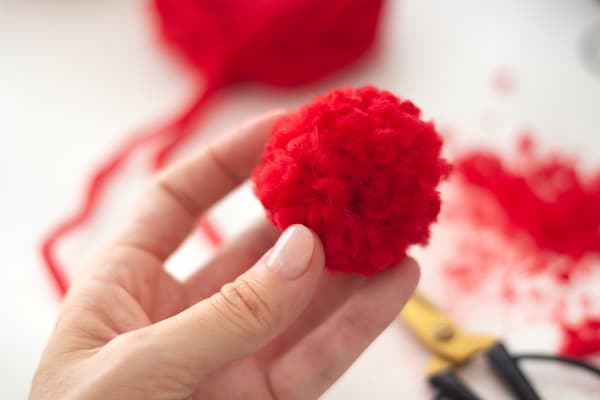 Eine Person hält ein rotes Wollknäuel in der Hand.
