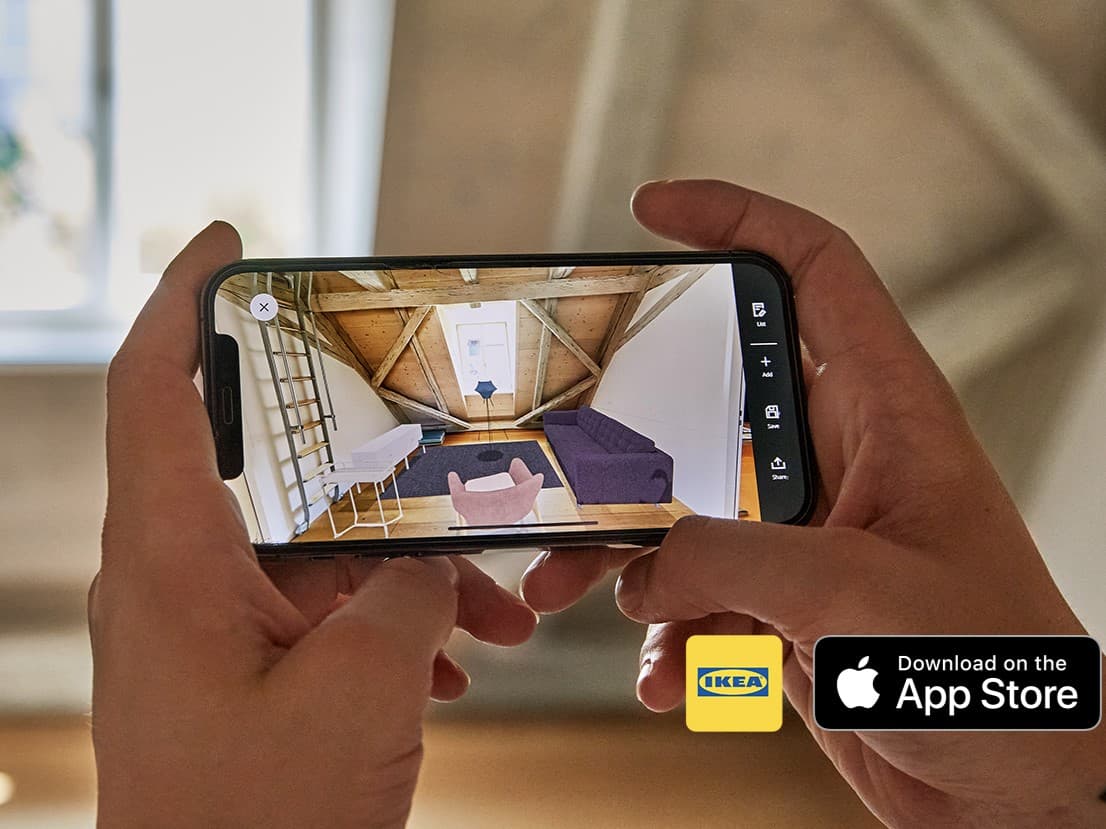 Eine Person hält ein Smartphone mit geöffneter IKEA App, die virtuell Möbel in einem Dachzimmer platziert – moderne Einrichtungsplanung mit Augmented Reality und App Store Download-Möglichkeit.

