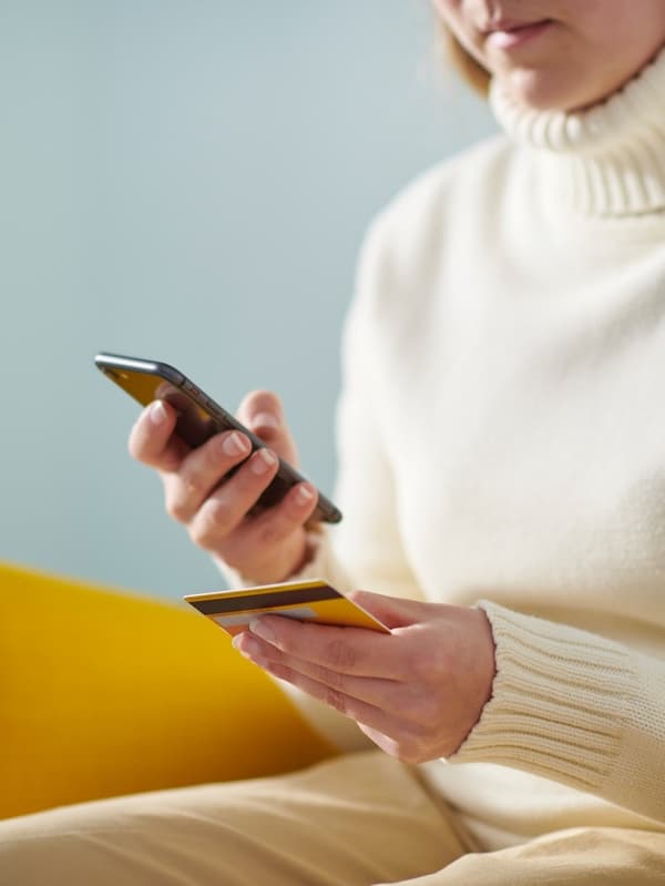 Eine Person hält eine Bankkarte in der einen und ein Smartphone in der anderen Hand. 