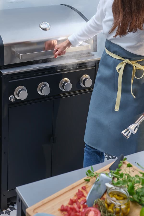 Eine Person hält eine Grillzange in der Hand und ist dabei, den Deckel des Gasgrills einer GRILLSKÄR Außenküche zu öffnen.