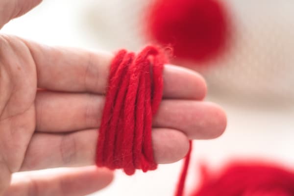 Eine Person hat rotes Garn um drei Finger gewickelt.