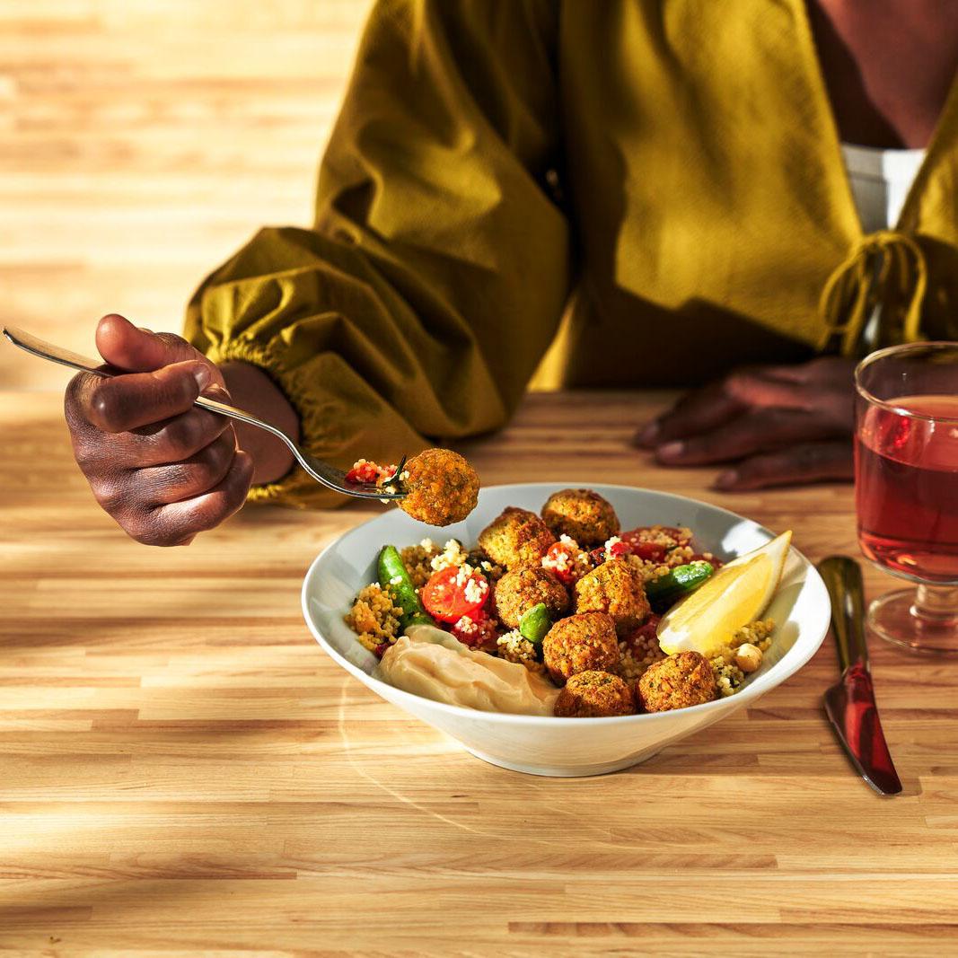 Eine Person isst Falafelbällchen mit Couscous und Aioli Sauce. Daneben steht ein Glas Saft.