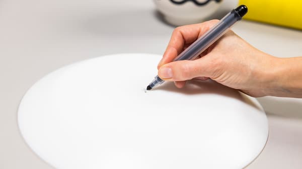 Eine Person markiert mit einem schwarzen Stift auf der Rückseite des Tellers die Mitte von diesem.