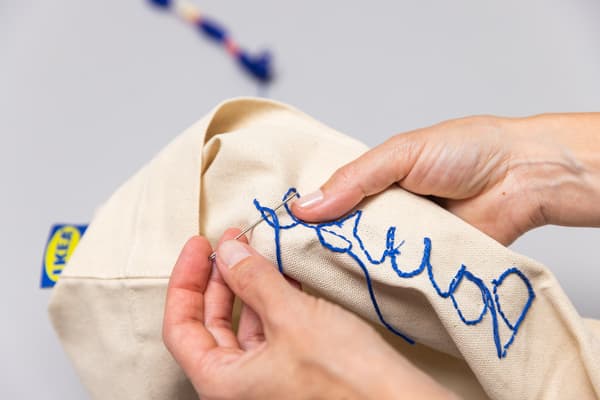 Eine Person näht mit blauem Stickgarn die Schrift nach.