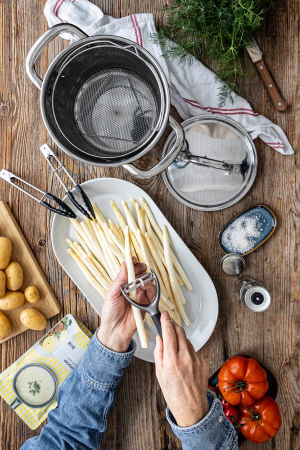Eine Person schält Spargel für das Rezept: Spargel mit Kartoffeln, geschmorten Tomaten und Zitronen-Dill-Soße.