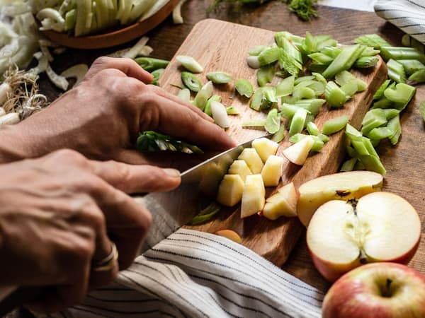 Eine Person schneidet Frühlingszwiebeln und Äpfel für das Rezept Plantbullar mit Linsen-Fenchel-Salat.