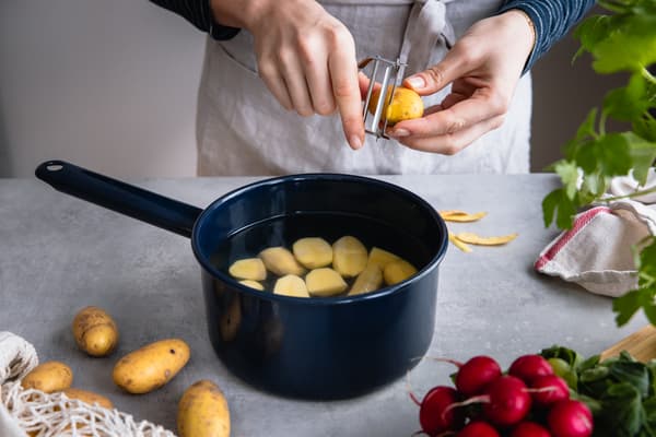 Eine Person schneidet Kartoffeln in einen Topf zum Kochen.