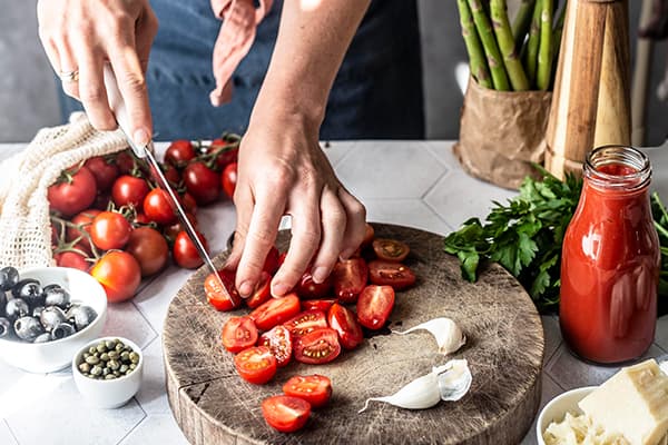 Eine Person schneidet Tomaten für das Rezept vegane Pasta alla Puttanesca mit grünem Spargel und IKEA Plantbullar.
