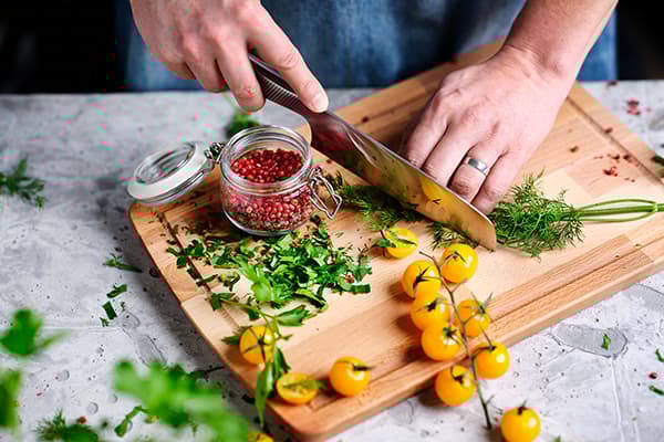 Eine Person schneidet Tomaten und Kräuter als Topping für vegetarische herzhafte Waffeln.