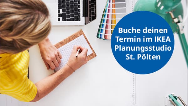 Eine Person schreibt mit einem Stift auf einen Notizblock an einem Schreibtisch, auf dem auch ein Laptop, Farbfächer und eine grüne Schreibtischlampe liegen. Rechts im Bild steht in einem blauen Kreis: „Buche deinen Termin im IKEA Planungsstudio St. Pölten“.