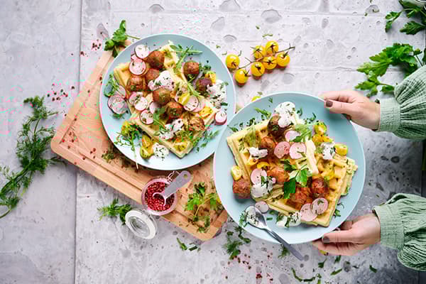 Eine Person serviert zwei Teller mit frischen vegetarischen herzhaften Waffeln.