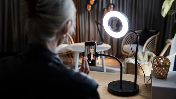 Eine Person sitzt an einem Schreibtisch und ist gerade dabei ein Video aufzunehmen. Dazu nutzt sie eine LÅNESPELARE Ringleuchte mit Mobiltelefonhalter.