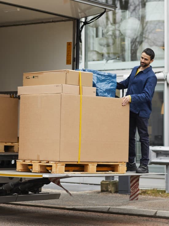 Eine Person steht auf der Rampe eines Lastwagens und hält ein Paket fest.
