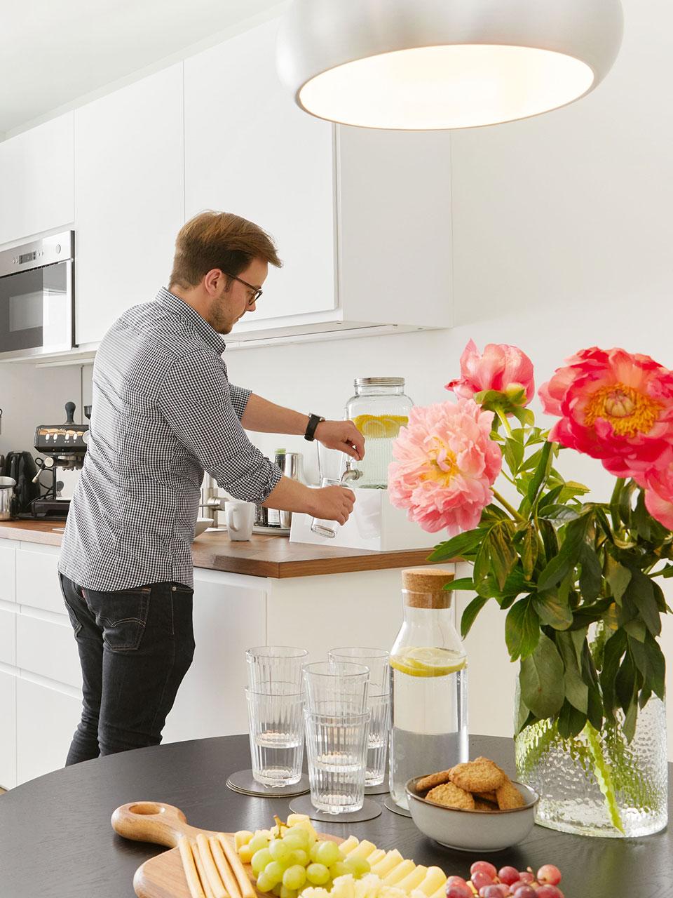 Eine Person steht in einer Kaffeeküche an einem Wasserspender und füllt ein Glas mit Wasser. 