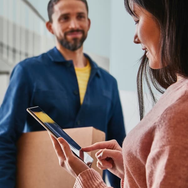 Eine Person übergibt einer anderen Person ein Paket im Hausflur. 