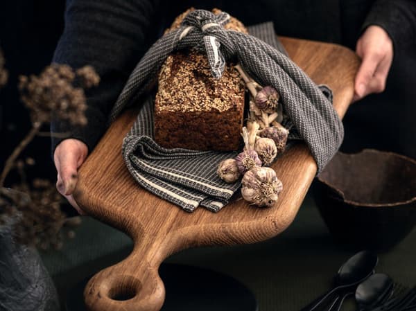 Eine Person überreicht einen Laib Brot auf einem Schneidebrett.