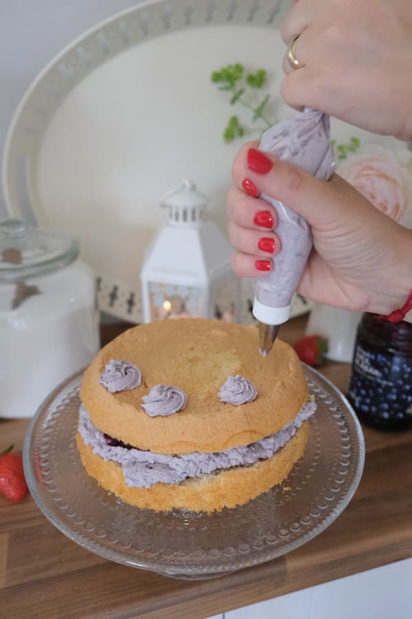 Eine Person verziert eine Blaubeer-Mascarpone-Torte.