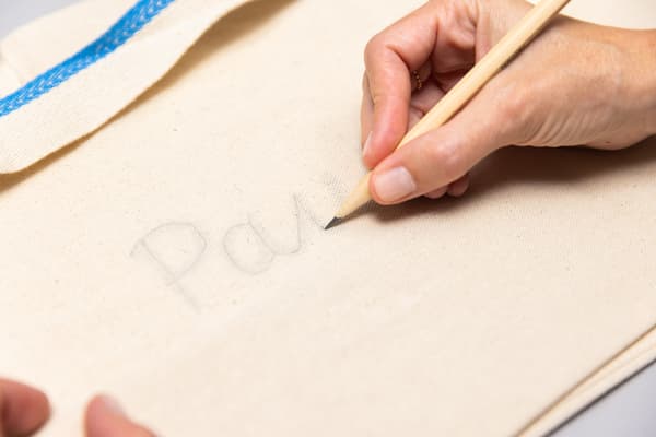 Eine Person zeichnet mit dem Bleistift etwas auf die Tasche.