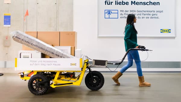 Eine Person zieht einen gelben E-Cargo Trailer auf dem Pakete liegen.
