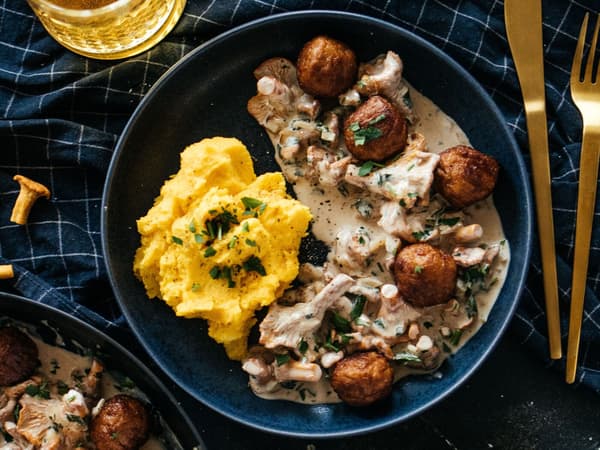 Eine Portion Plantbullar in Pfifferling-Rahm-Sauce ist auf einem blauen Teller angerichtet.