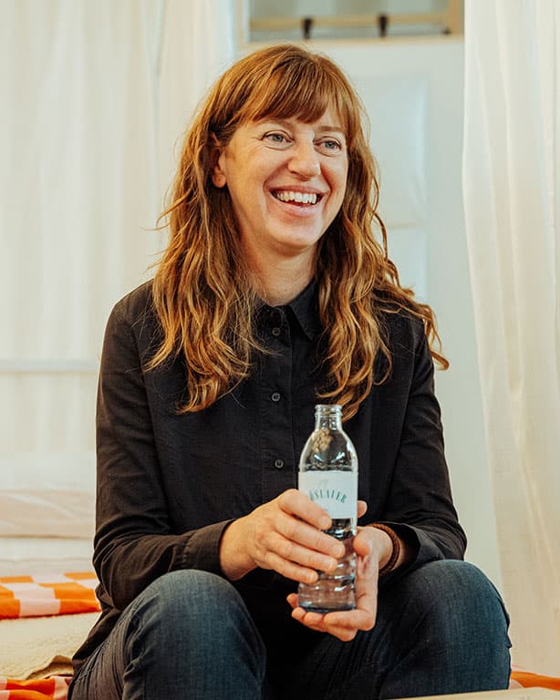 eine rothaarige Frau mit dunkler Kleidung die eine Wasserflasche hällt.