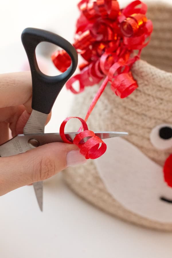 Eine Schere fährt durch das rote Geschenkband, um es wie Locken zu kräuseln. 