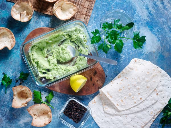 Eine Schüssel mit Avocadocreme, daneben weitere Zutaten für das Rezept herzhafte Tortilla Muffins mit Tomate & Avocado.