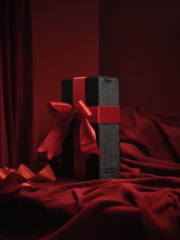 Eine schwarze SYMFONISK Box mit einer roten Schleife, die auf rotem Seidenstoff steht.