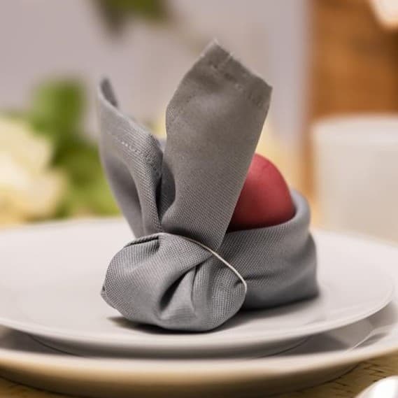 eine Serviette ist wie ein Osterhase geformt und hat hinten drinnen ein rotes Ei.