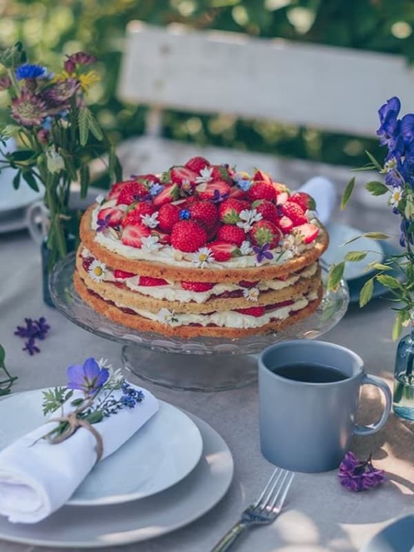 Eine sommerliche Mandeltorte mit Erdbeeren und Sahne steht auf einem gedeckten Tisch