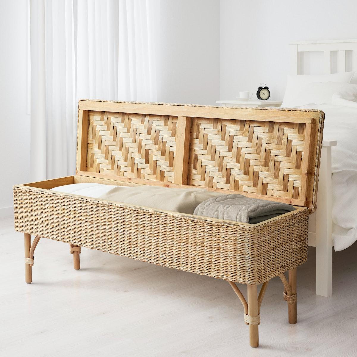 eine Stohgeflochtene Wäschekiste in einem Schlafzimmer vor einem weißen Bett.