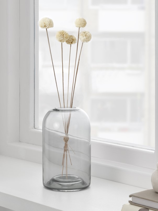 Eine Vase mit Trockenblumen steht auf einem weißen Fensterbrett