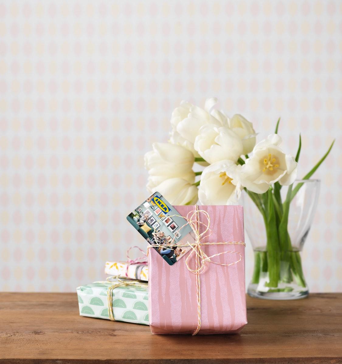Eine Vase mit weißen Blumen und eingepackte Geschenke mit einer IKEA Geschenkkarte.