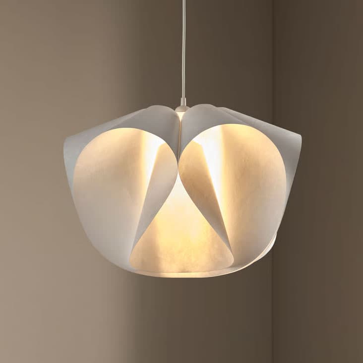 Eine warm leuchtende BACKNÄTE Hängeleuchte im Fokus vor einer beigen Wand