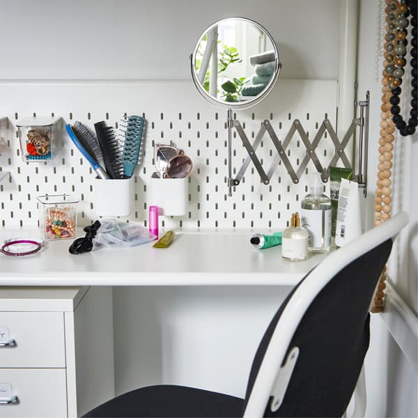 Eine weisse Arbeitsplatte unter einem Hochbett, u. a. mit einem FRÄCK Spiegel an der Wand. Utensilien für Make-up und Frisur finden sich an den Fächern der Lochplatte.
