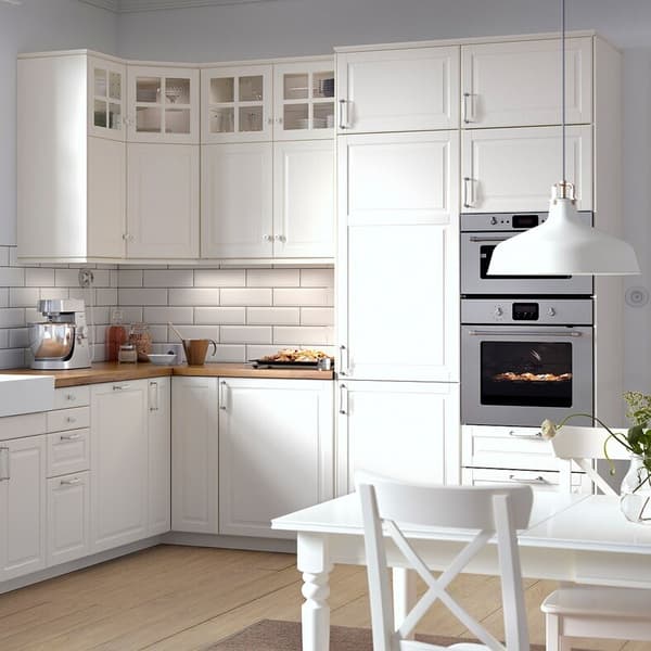 Eine weiße BODBYN Küche mit Holzarbeitsplatte, Hängeschränken darüber und einem Hochschrank mit eingebautem Backofen.
