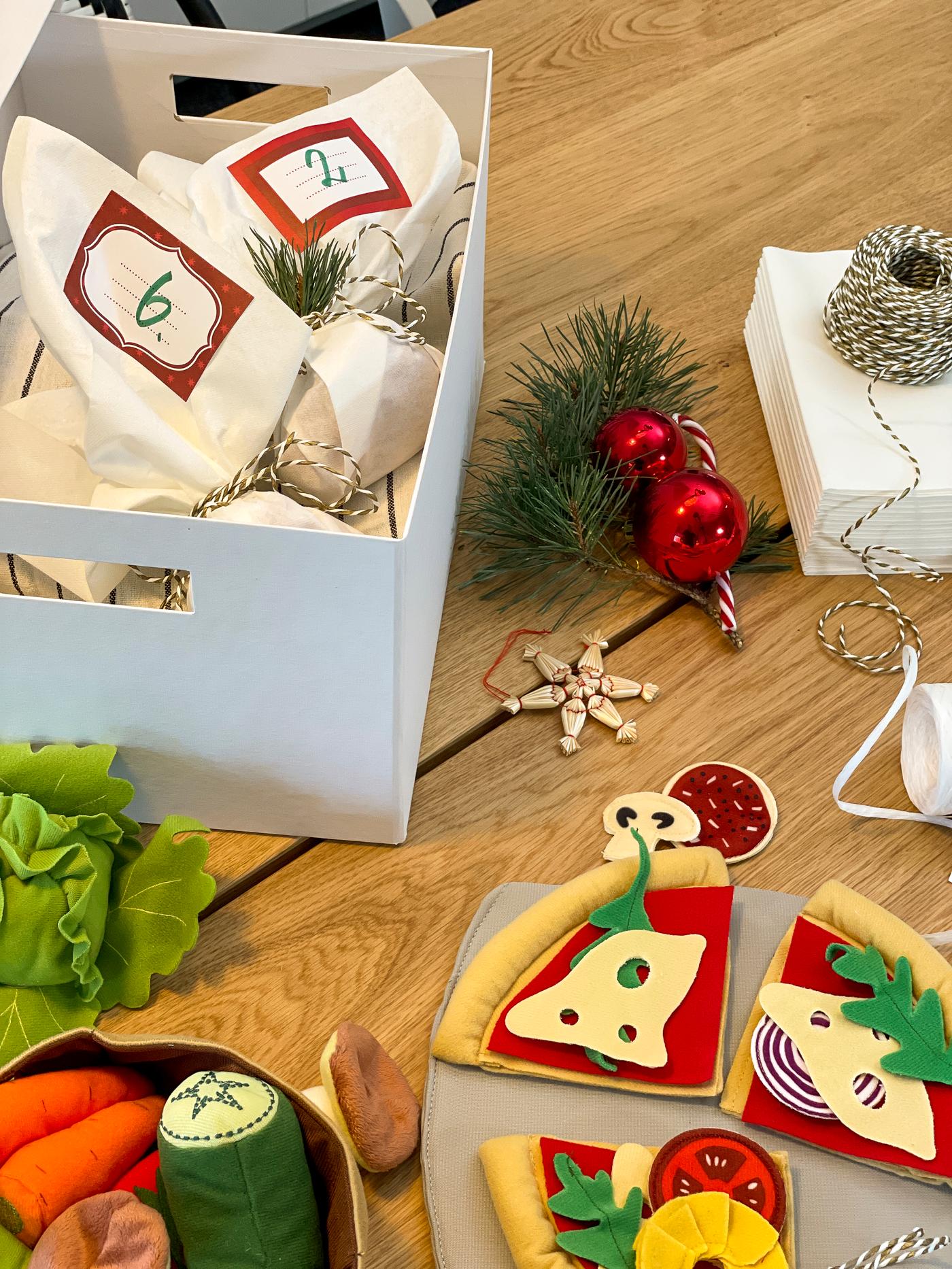 Eine weiße Kiste mit kleinen Päckchen für einen Adventskalender auf dem Tisch. DUKTIG Spielpizza.